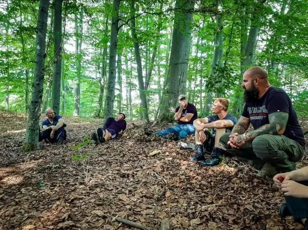 Gruppe sitzt auf dem Waldboden und diskutiert in einer lichtdurchfluteten Waldlandschaft