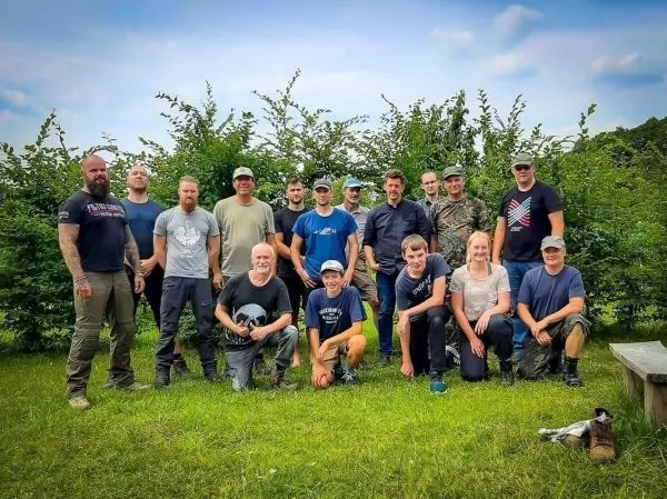 Gruppe von Personen steht auf einer Wiese vor Büschen