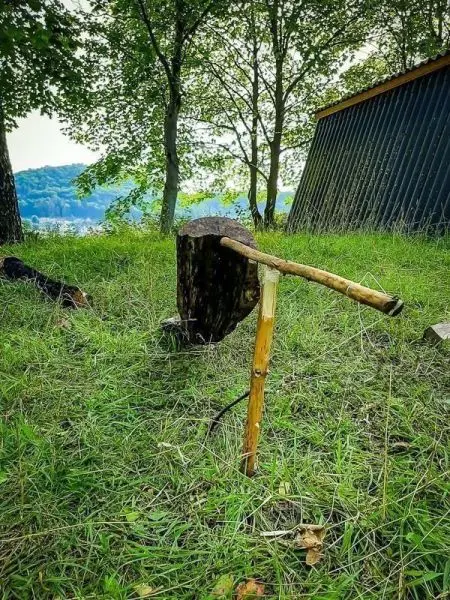 Holzstück steht aufrecht, mit improvisierter Axt aus einem Stock und einem weiteren Holzstück