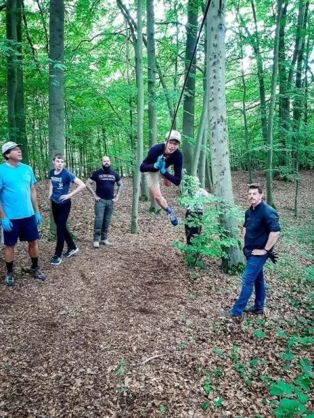 Junge schwingt an Seilbrücke zwischen Bäumen, Zuschauer beobachten im Wald