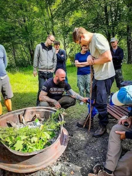 Mann demonstriert Techniken zur Feuerbereitung mit einem Stock vor einer Gruppe