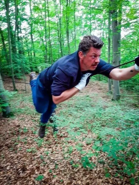 Mann führt eine Seilquerung zwischen Bäumen im Wald durch