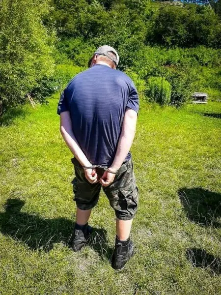 Mann mit Handschellen hinter dem Rücken steht auf einer Wiese