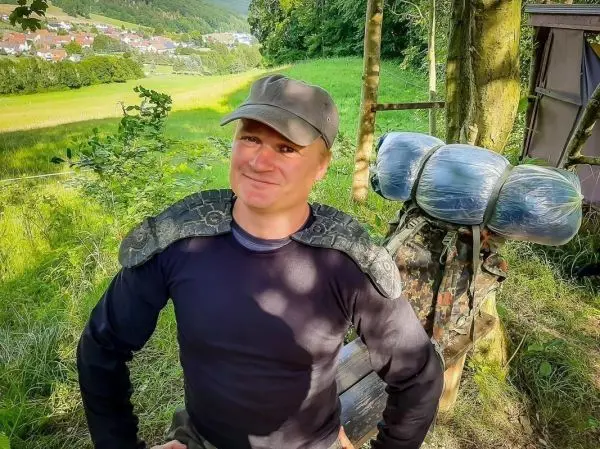 Mann mit Rucksack und Schlange auf der Schulter steht in der Natur