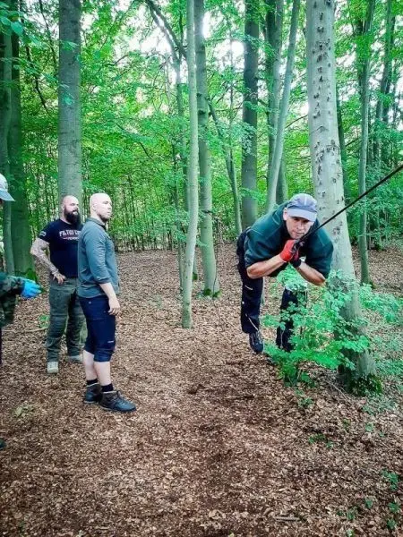 Mann schwingt an einem Seil zwischen Bäumen im Wald, während andere zuschauen