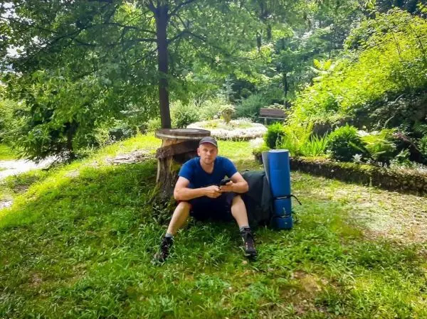 Mann sitzt auf dem Gras neben einem Rucksack und einer Isomatte