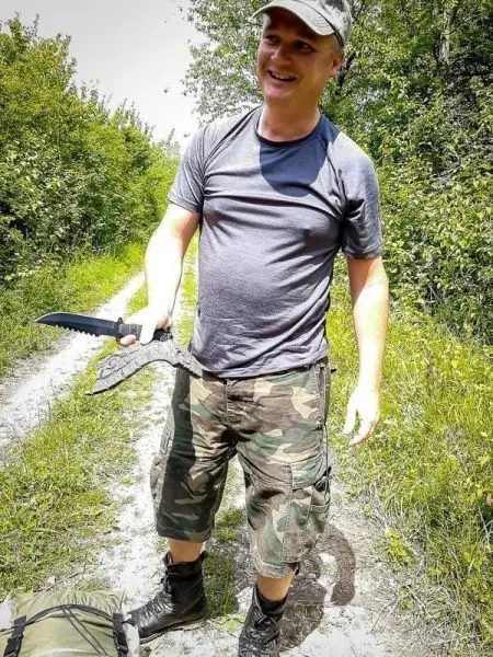 Person hält ein großes Messer und lächelt auf einem Weg