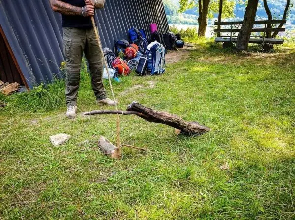 Person hält einen Stock über einem Holzstück im Gras