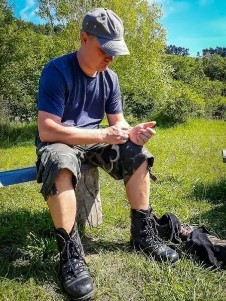 Person sitzt auf einem Baumstumpf und schnürt Stiefel