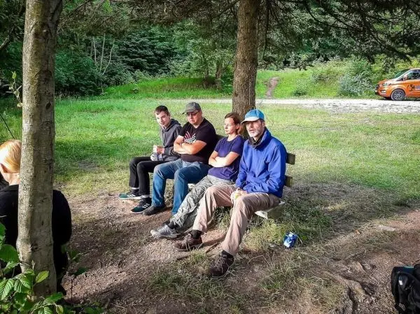 Vier Personen sitzen auf einer Bank unter Bäumen in einer grünen Umgebung