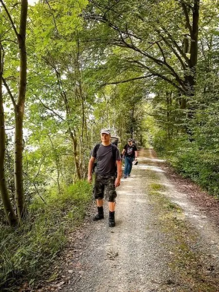 Wanderer auf einem Schotterweg umgeben von Bäumen und Grün