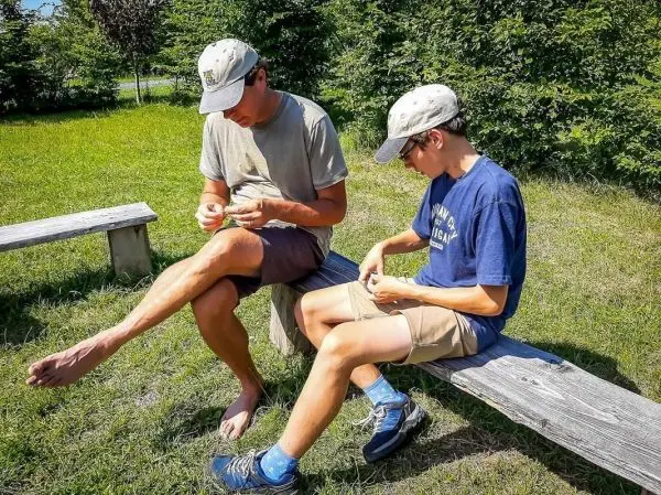 Zwei Personen sitzen auf einer Bank und knoten Schnüre zusammen