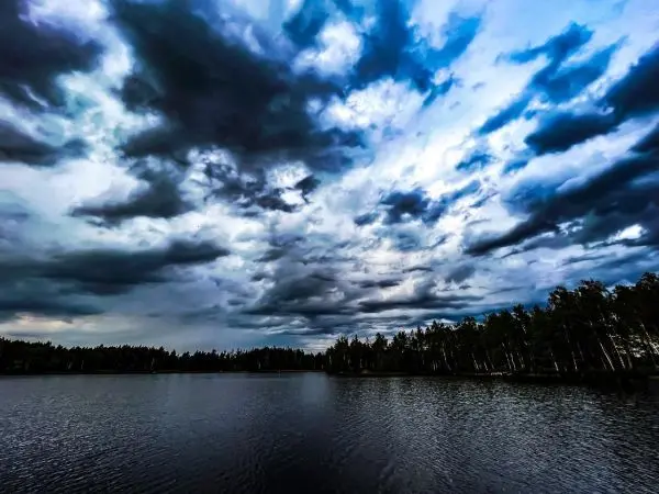 Dunkle Wolken spiegeln sich im ruhigen Wasser eines Sees