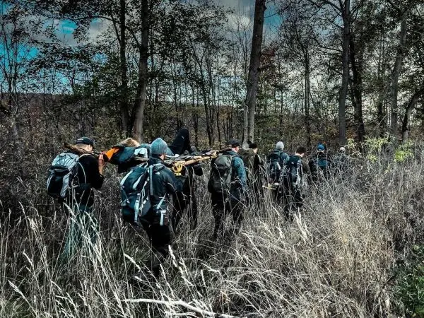 Gruppe trägt improvisierte Trage durch hohes Gras im Wald