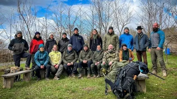 Gruppe von Personen in Outdoor-Bekleidung sitzt und steht auf einer Wiese