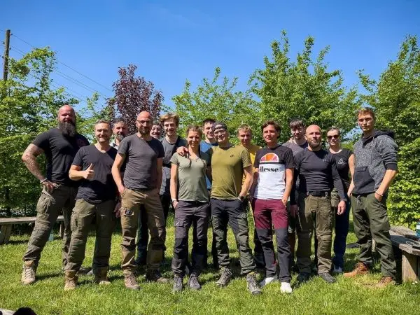 Gruppe von Personen in Outdoor-Bekleidung steht auf einer Wiese zwischen Bäumen