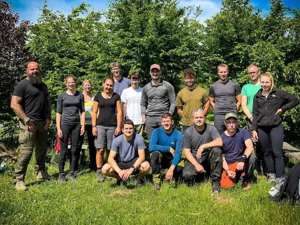 Gruppe von Personen in Outdoor-Bekleidung steht vor einer grünen Hecke