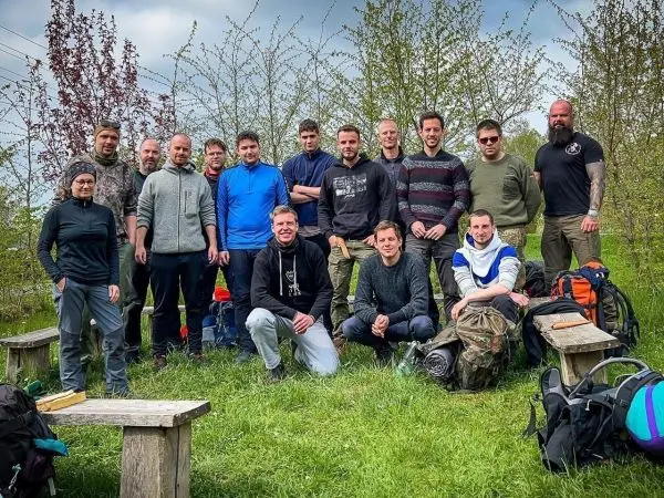 Gruppe von Personen mit Rucksäcken auf einer Wiese vor Bänken