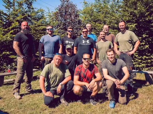 Gruppe von Personen posiert im Freien vor einer grünen Hecke
