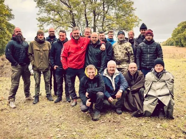 Gruppierung von Personen in Outdoor-Bekleidung auf einer Wiese unter Bäumen