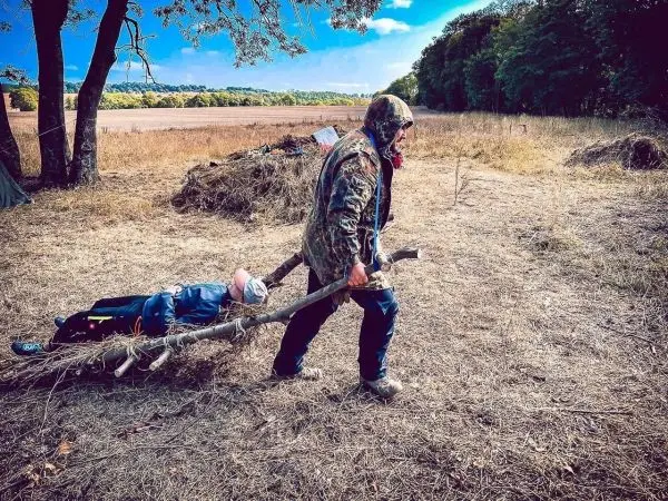 Holzstamm dient als improvisierte Trage für eine liegende Person im Freien