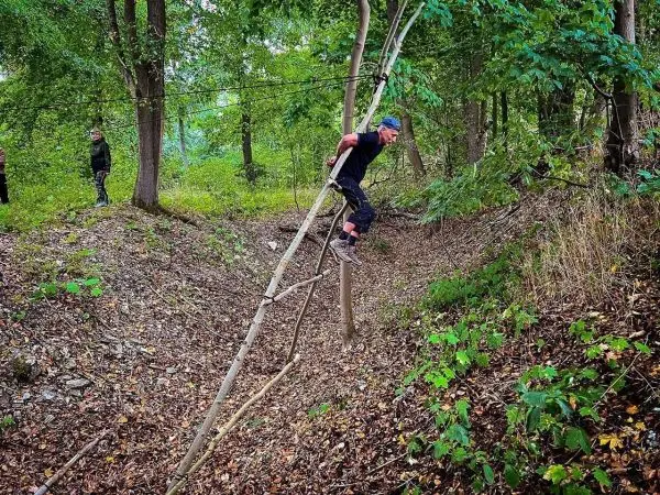 Person balanciert auf einer selbstgebauten Seilbrücke im Wald