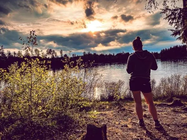 Person steht am Ufer eines Sees und betrachtet den Sonnenuntergang