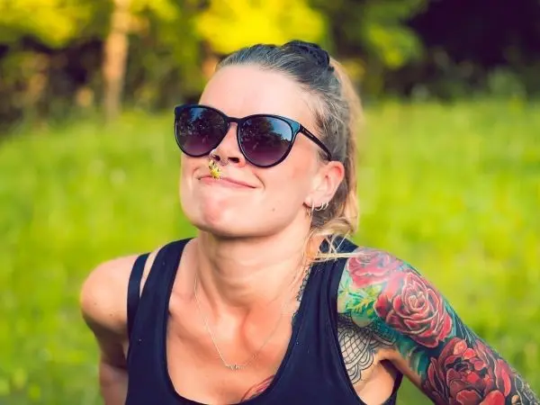 Person trägt Sonnenbrille und lächelt mit einer Blume im Mund