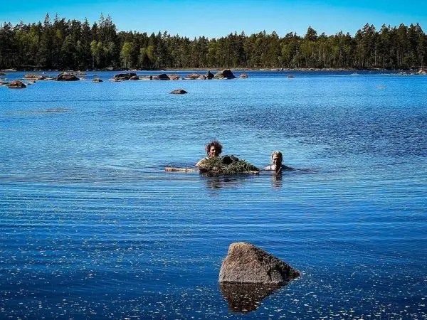 Zwei Personen schwimmen im klaren Wasser eines Sees, umgeben von Felsen und Bäumen