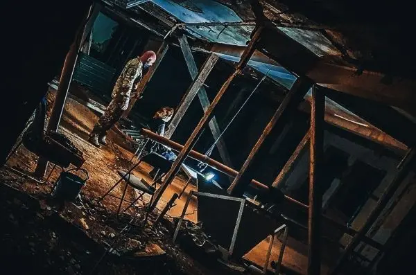 Zwei Personen stehen in einem verlassenen, dunklen Raum mit beschädigter Decke