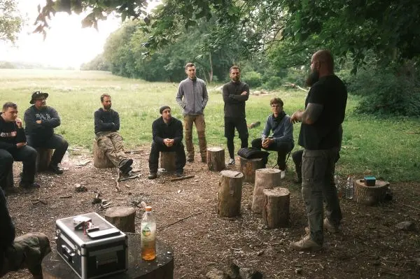 Ein Referent erklärt Techniken im Freien, während Teilnehmer auf Baumstümpfen sitzen