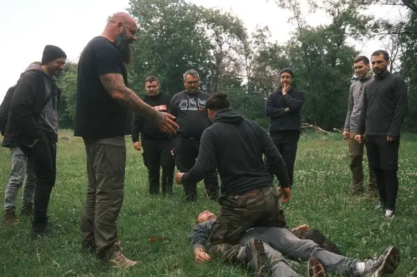 Ein Teilnehmer demonstriert eine Technik auf einem am Boden liegenden Mann, während andere zuschauen