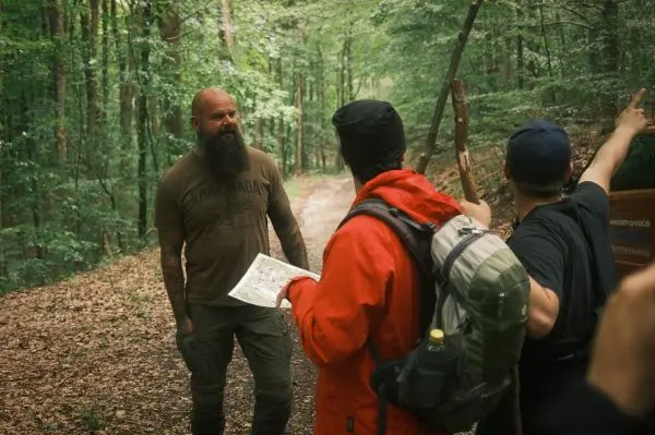 Eine Gruppe diskutiert mit einer Karte im Wald, während einer auf einen Weg zeigt