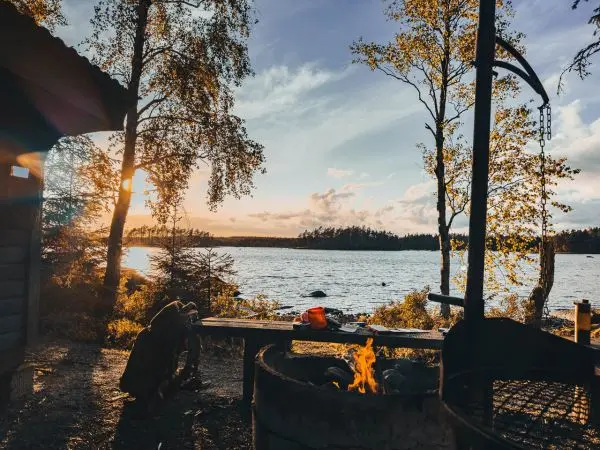 Feuer brennt in einem Grill, während die Sonne über dem Wasser untergeht