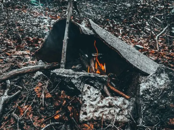 Feuer brennt unter einer improvisierten Steinunterkunft im Wald