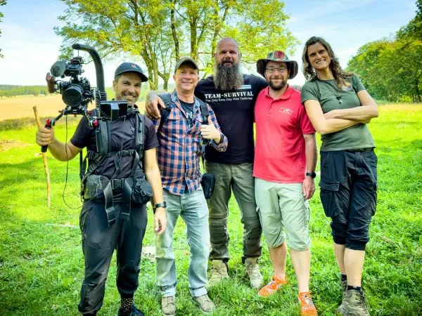 Fünf Personen stehen auf einer Wiese, einer hält eine Kamera mit Stativ