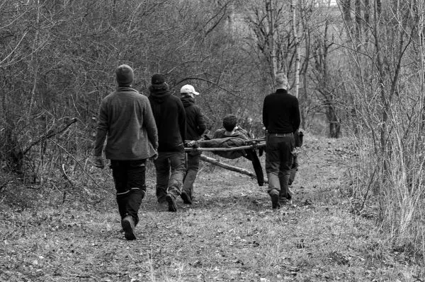 Fünf Personen tragen eine improvisierte Trage durch einen Waldweg