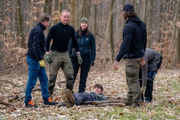 Gruppe arbeitet an improvisierter Trage aus Ästen für verletzte Person im Wald