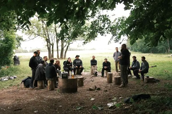 Gruppe sitzt auf Baumstümpfen und hört einem Redner im Freien zu