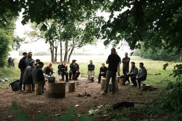 Gruppe sitzt auf Baumstümpfen und hört einem Vortrag im Freien zu