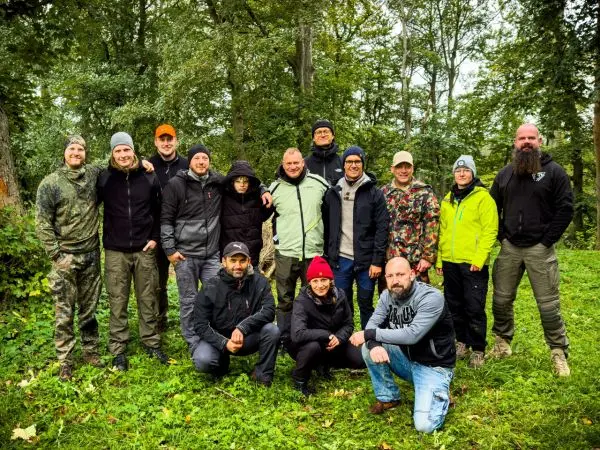 Gruppe von Personen in Outdoor-Bekleidung steht auf einer Wiese im Wald