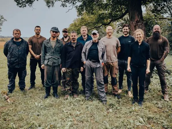 Gruppe von Personen in Outdoor-Bekleidung steht auf einer Wiese unter einem Baum