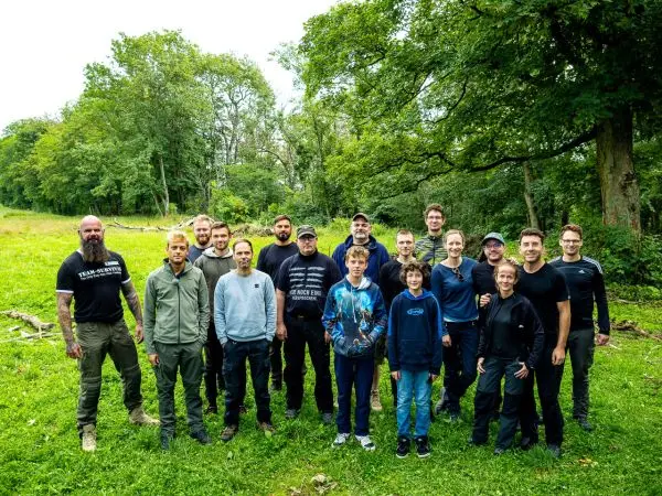 Gruppe von Personen steht auf einer Wiese umgeben von Bäumen