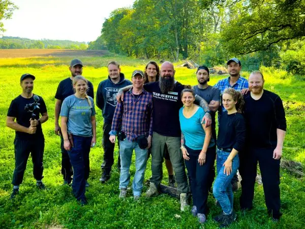 Gruppe von Personen steht auf einer Wiese, umgeben von Bäumen und Feldern