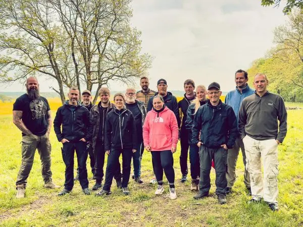 Gruppe von Personen steht auf einer Wiese vor Bäumen