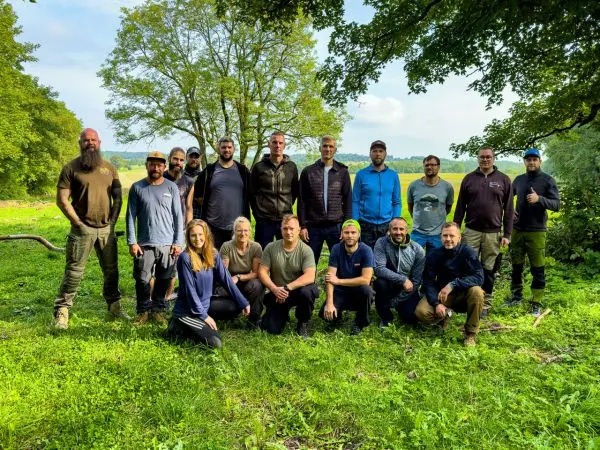 Gruppe von Personen steht auf einer Wiese vor Bäumen und einem Feld