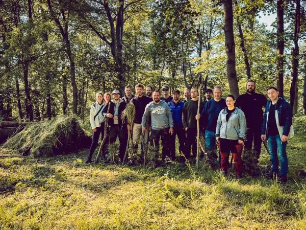 Gruppe von Personen steht im Wald, einige halten Stöcke oder Werkzeuge