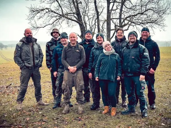 Gruppe von zehn Personen steht auf einer Wiese unter Bäumen