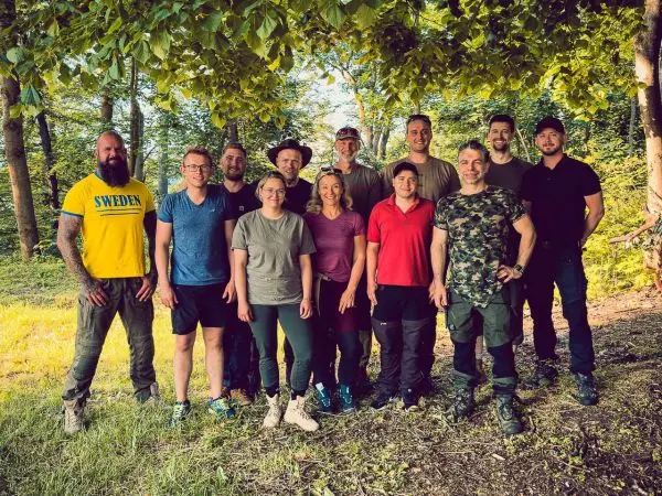 Gruppe von zwölf Personen steht im Freien unter Bäumen