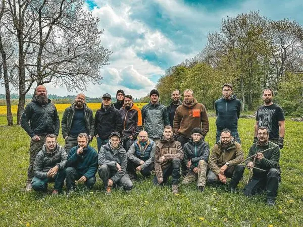 Gruppierung von Personen im Freien auf einer Wiese, umgeben von Bäumen und Wolken